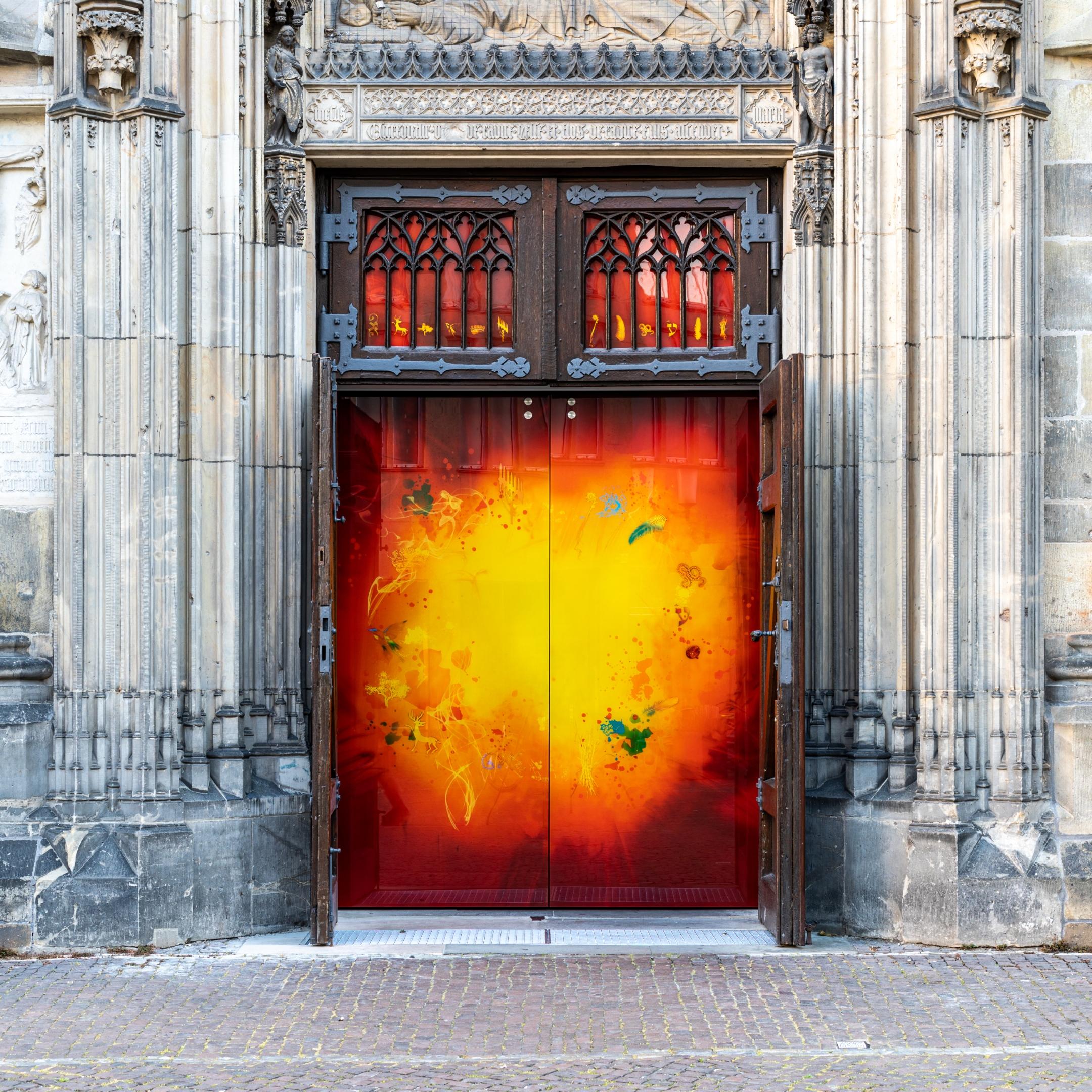 Glaskunstwerk „L’Or“ (René Blättermann, 2022) als Tür im Wurzel-Jesse-Portal der St.-Lamberti-Kirche in Münster, Nordrhein-Westfalen, Deutschland Der Entwurf des Glaskunstwerks stammt von René Blättermann unter theologischer Beratung von Almuth Jürgensen. Umgesetzt wurde der Entwurf von der Päpstlichen Hofglasmalerei DERIX GLASSTUDIOS in Taunusstein unter Leitung von Olaf Hanweg. Das Motiv zeigt um das „göttliche Licht“ 12 Symbole: Tempel, Hirsch, Spross, Vögel, Krone, Menora, Lamberti, Tamar, Nechuschtan, Ajin, Cherubim und Bündel.